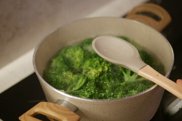 Boiling broccoli in a pot with a wooden spoon on the stove, preparing a healthy meal