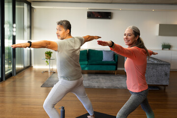 At home, diverse senior couple practicing yoga together in bright living room