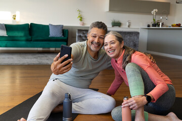 At home, diverse senior couple smiles for selfie on yoga mats in living room