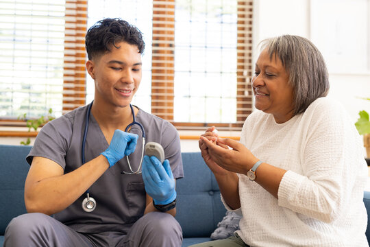 At home, biracial male nurse showing glucometer to senior female patient