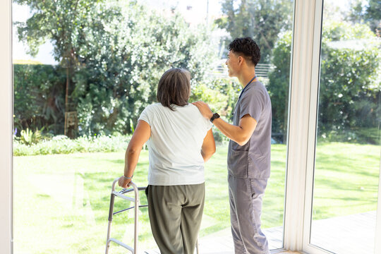 At home, a biracial male nurse aids a senior female patient with a walker