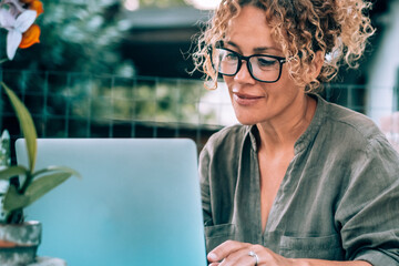 One modern happy serene woman using computer outdoor at home in garden. Pretty female writing on...