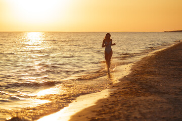 Silhouetted woman running on beach at sunset, wearing blue swimsuit, enjoying peaceful evening. High-quality beach vibes photo design for advertising, and social media, vlog