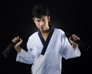 A male taekwondo athlete in a white taekwondo uniform stands posing with his hand holding a black belt