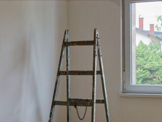 Wooden ladders stained with paint next to a window in the room next to freshly white-painted walls