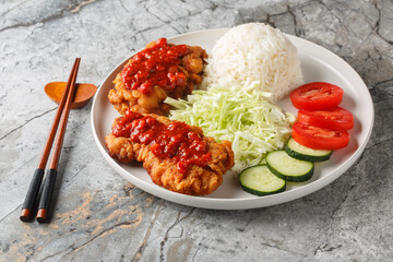 Ayam Geprek Sambal Bawang crispy fried chicken served with white rice, cucumber, tomato and cabbage closeup on the plate on the table. Horizontal