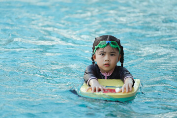 A young girl is in the water on a yellow surfboard. She is wearing a black and white swimsuit and...