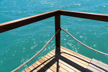Wooden pier with posts and ropes with sparkling sea water. Wooden pier with blue sea background.