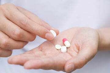 close up hand man taking multiple pills take a medicine in hand holding a cup glass of drinking water on wooden table. Stop drug use Taking Medication health care medical concept..