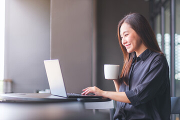 Portrait image of a young woman drinking coffee while working on laptop computer in cafe