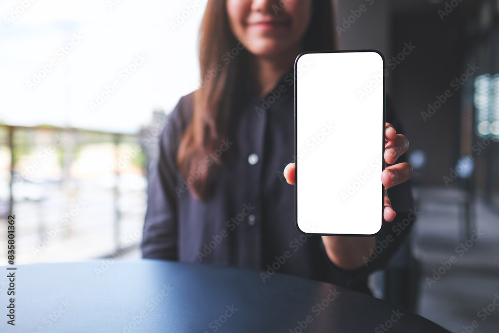 Wall mural Mockup image of a young woman holding and showing a mobile phone with blank white screen