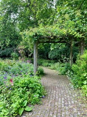 An English Garden with a pergola and lush spring flowers, grass and a cobblestone pathway.  Taken during the day, no people.