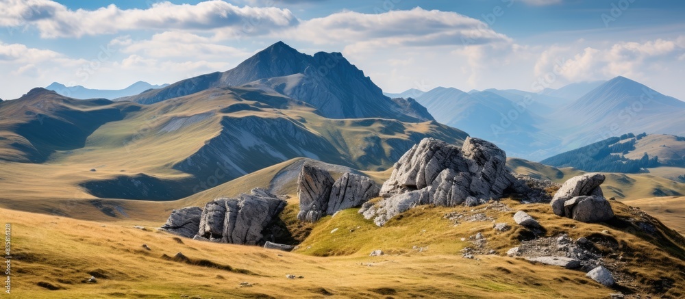 Poster Scenic view of yellow fall grass on a mountainside with beautiful rock formations against a blue sky with clouds, ideal for a copy space image.