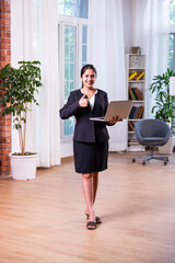 Asian Indian corporate woman professional using laptop while standing near window in office