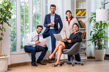 Candid group portrait of young Indian asian business professionals sitting near office window...