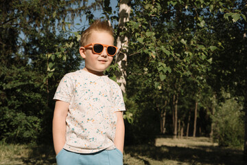 Happy child in sunglasses in the forest against the background of green trees. Close-up. Happy boy with glasses enjoying the sun. Vacation, summer vacation concept. High quality photo