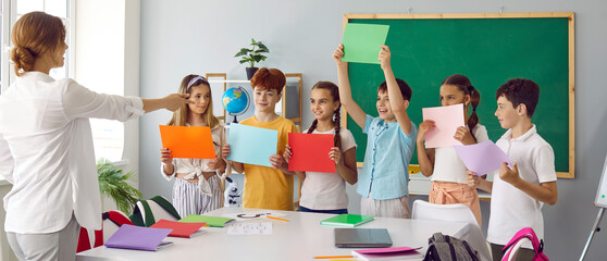 Elementary school students showing blank paper sheets to teacher in classroom. Group of cute...