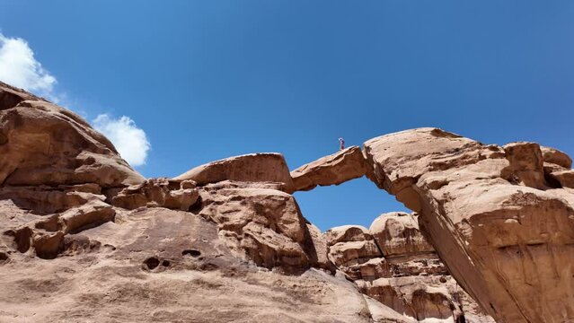 tourist woman walking atop the famous Um Fruth rock arch in the vast Wadi Rum desert, Jordan, admiring the expansive sandy landscape under a clear blue sky