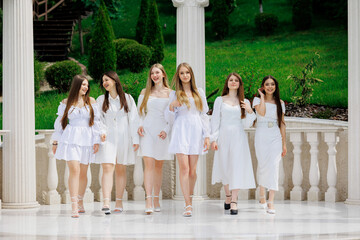 A group of women in white dresses are posing for a photo. Scene is lighthearted and fun, as the women are all smiling and enjoying themselves. The setting is a courtyard or garden