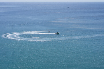Naklejka premium The turn of the yacht in the form of a loop and tourists engaged in water tubing it happens at a great distance (Rhodes, Greece)