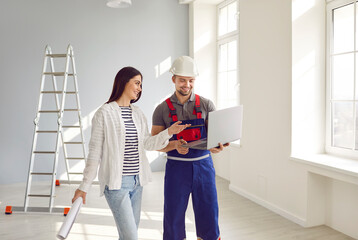 Woman apartment owner discussing design construction plan with contractor. Builder in hardhat and uniform showing project of renovation to young woman using computer. Building, home renovation