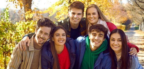 Close up portrait of group of happy friends walking in autumn park and hugging. Young smiling...