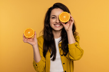 Merry young lady posing for the camera with citrus fruit halves against the yellow background in...