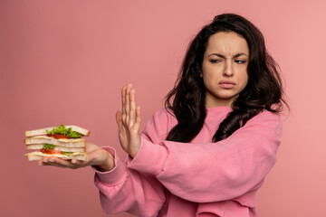 Displeased young dark-haired female showing her food aversion during the studio photo shoot on the...