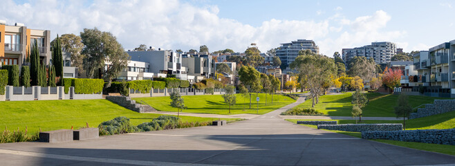 Panoramic urban landscape of a large park with concrete footpath and landscaped plants and grass...