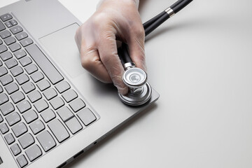 Hand with stethoscope on laptop, closeup. Concept of technical support