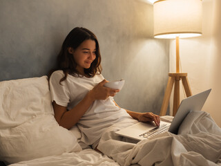 Young woman enjoying breakfast in bed while watching something on a laptop. Cozy morning setup with...