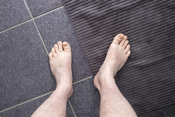 Men's feet on a bath towel in the bathroom on a dark floor