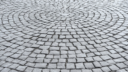 Gray cobblestone pavement arranged in intricate circular pattern. Detailed texture of stone surface highlights geometric design and traditional craftsmanship