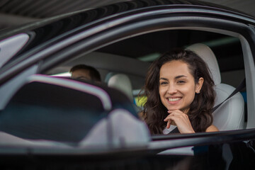 Happy young woman fastened with a seat belt traveling with her boyfriend by car, looking at side view mirror. Travel adventure drive, happy summer vacation concept