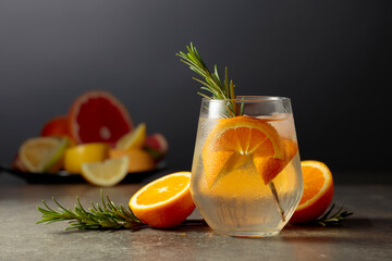 Cocktail gin tonic with ice, rosemary, and orange on a stone table.