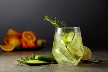 Cocktail gin tonic with ice, rosemary, lime, and cucumber on a stone table.