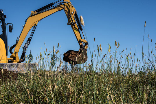Yellow excavator carrying bucket of dirt across grassy paddock field