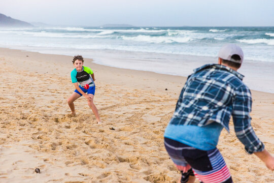 Son throwing ball to father on beach playing cricket