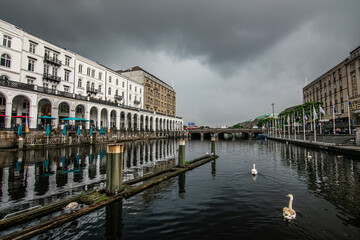 Naklejka premium Swans swim in the waters by the colonnades of Hamburg, with clouds looming overhead