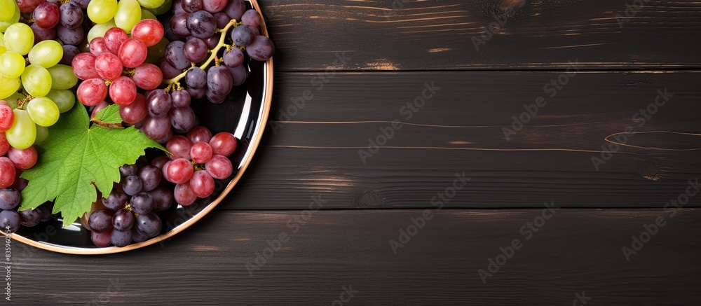 Poster top view of various types of grapes on vintage plate on black wooden surface. creative banner. copys