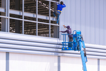 Construction workers with articulated boom lift installing aluminum corrugated steel sheets on...