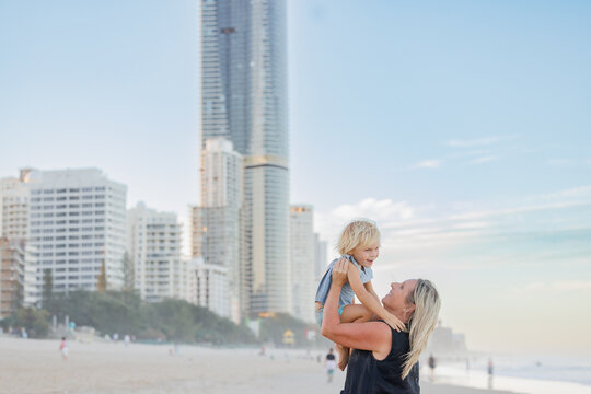 Mother lifting son in the air on Surfers Paradise beach with skyscrapers in background