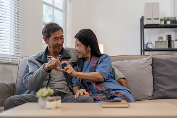 Healthy elderly couple making heart shape with hands on couch, Concept of love and companionship