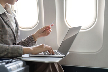 Businesswoman using laptop and credit card for online purchase while seated in airplane