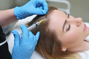 A dermatologist cosmetologist performs a mesotherapy procedure and injects an injection into the scalp of a young woman patient.