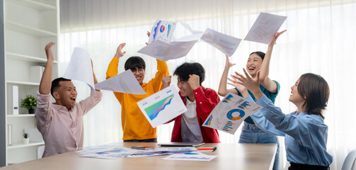 Excited and happy startup company employee celebrate and throw paper in the air after make...