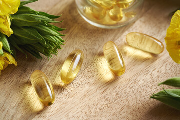 Gel capsules of evening primrose oil with blooming Oenothera biennis plant