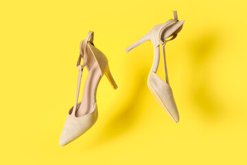 Stylish female shoes flying against yellow background