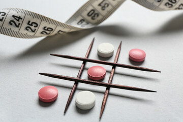 Tic tac toe game with pills, toothpicks and measuring tape on grey background, closeup