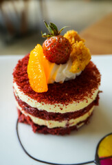 Red velvet cake, classic three layered cake from red butter sponge cakes with cream cheese frosting, with mandarin orange and candied strawberry as topping American cuisine